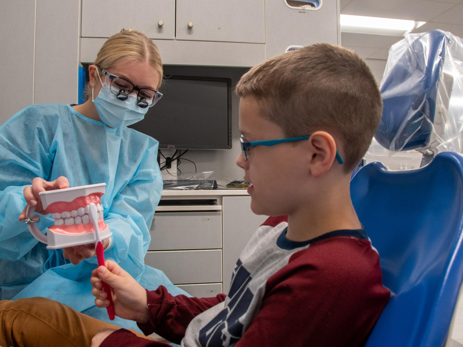 A dental hygiene student shows a young paitent how to use a toothbrush