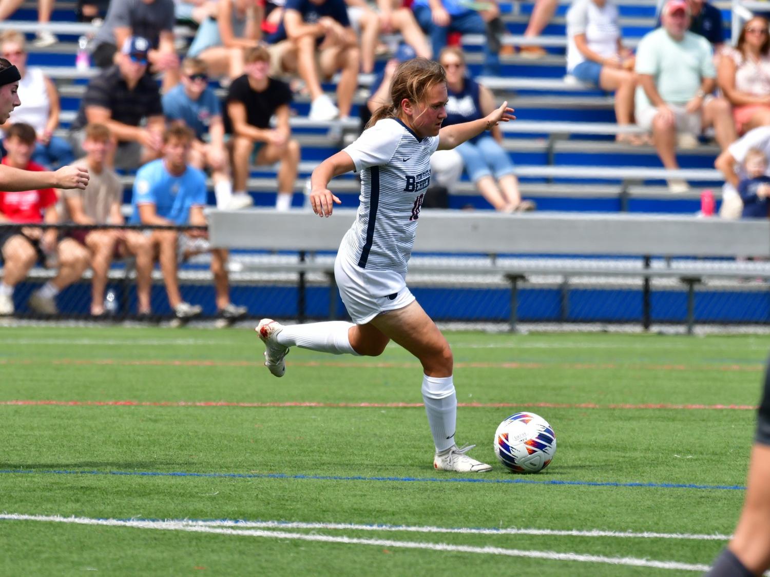 A female Penn State Behrend soccer player advances with the ball.