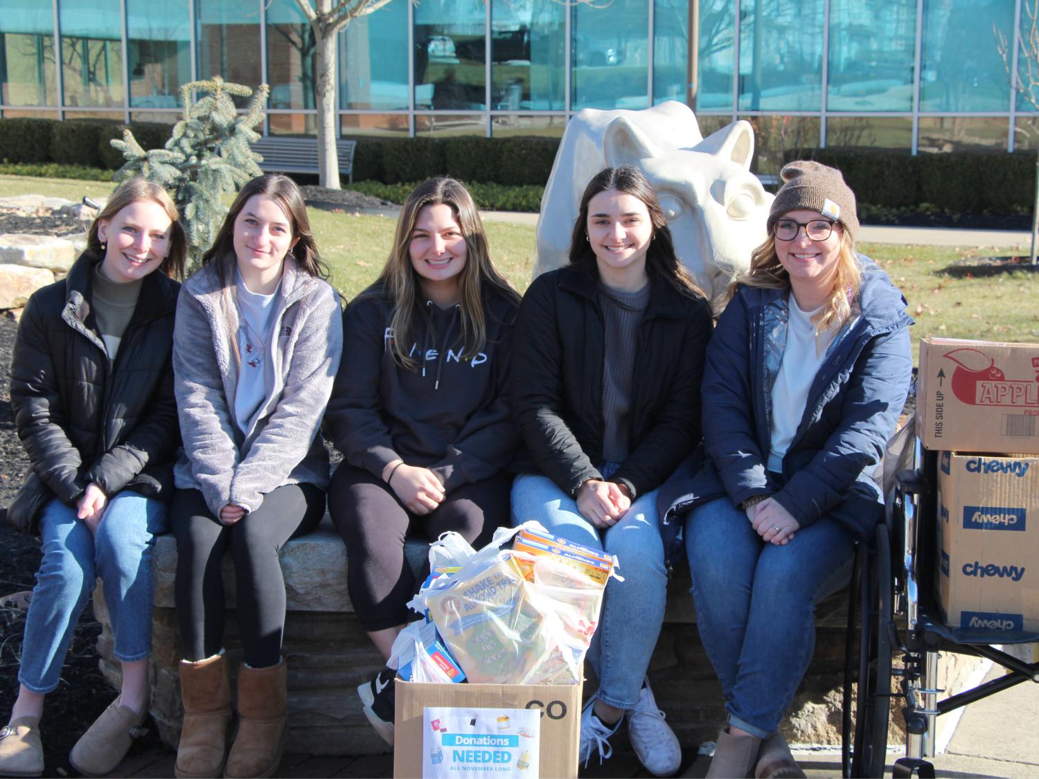 Five people in front of the lion shrine with boxes of food.