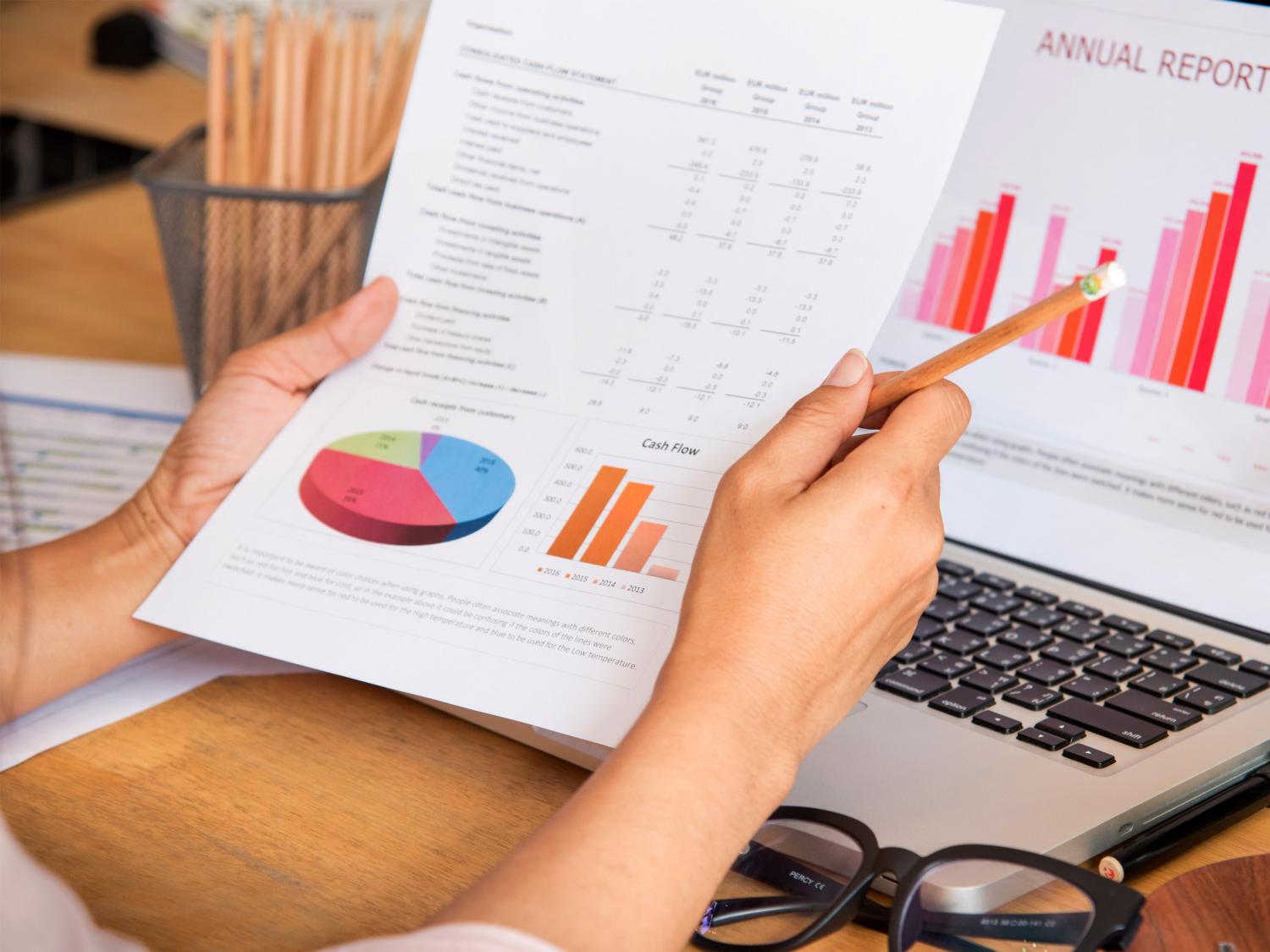 A woman reviews information on an Excel spreadsheet, with graphs, both on paper and on a computer screen.