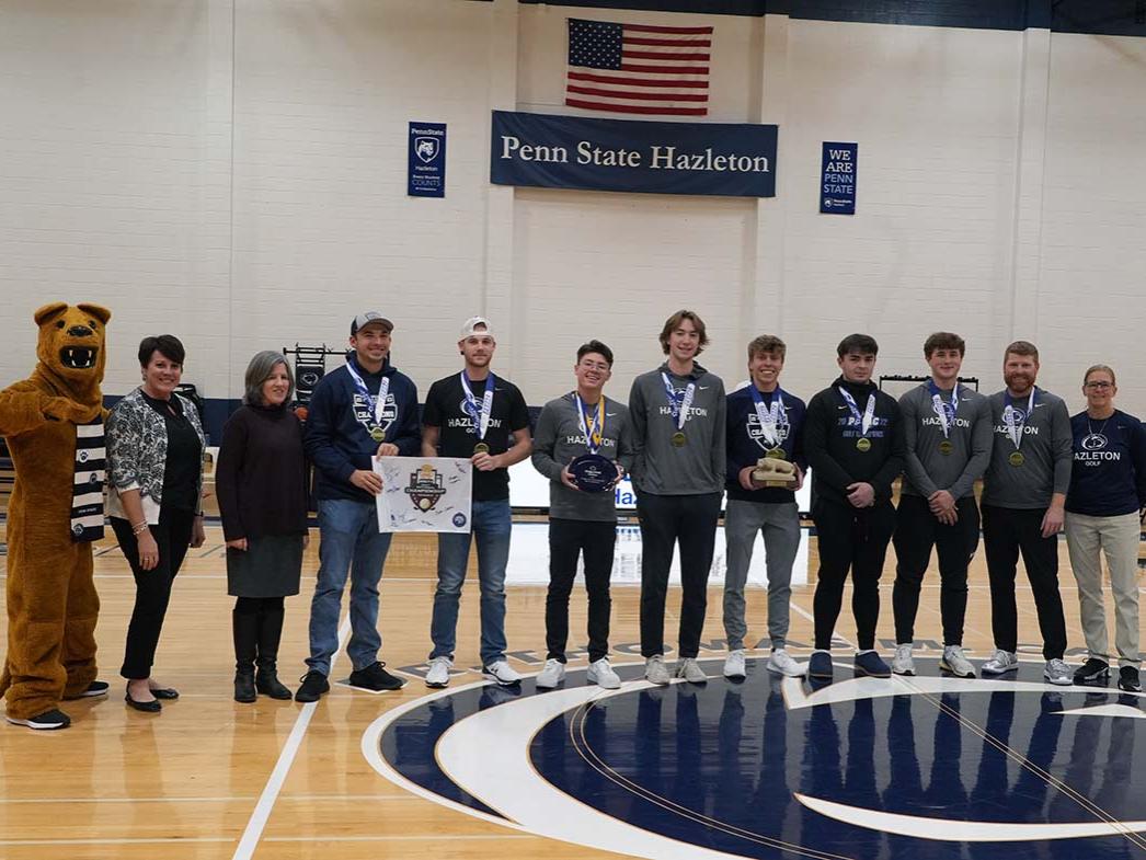 Group of 12 people lined up in a row on a basketball court with seven of them wearing championship medals.