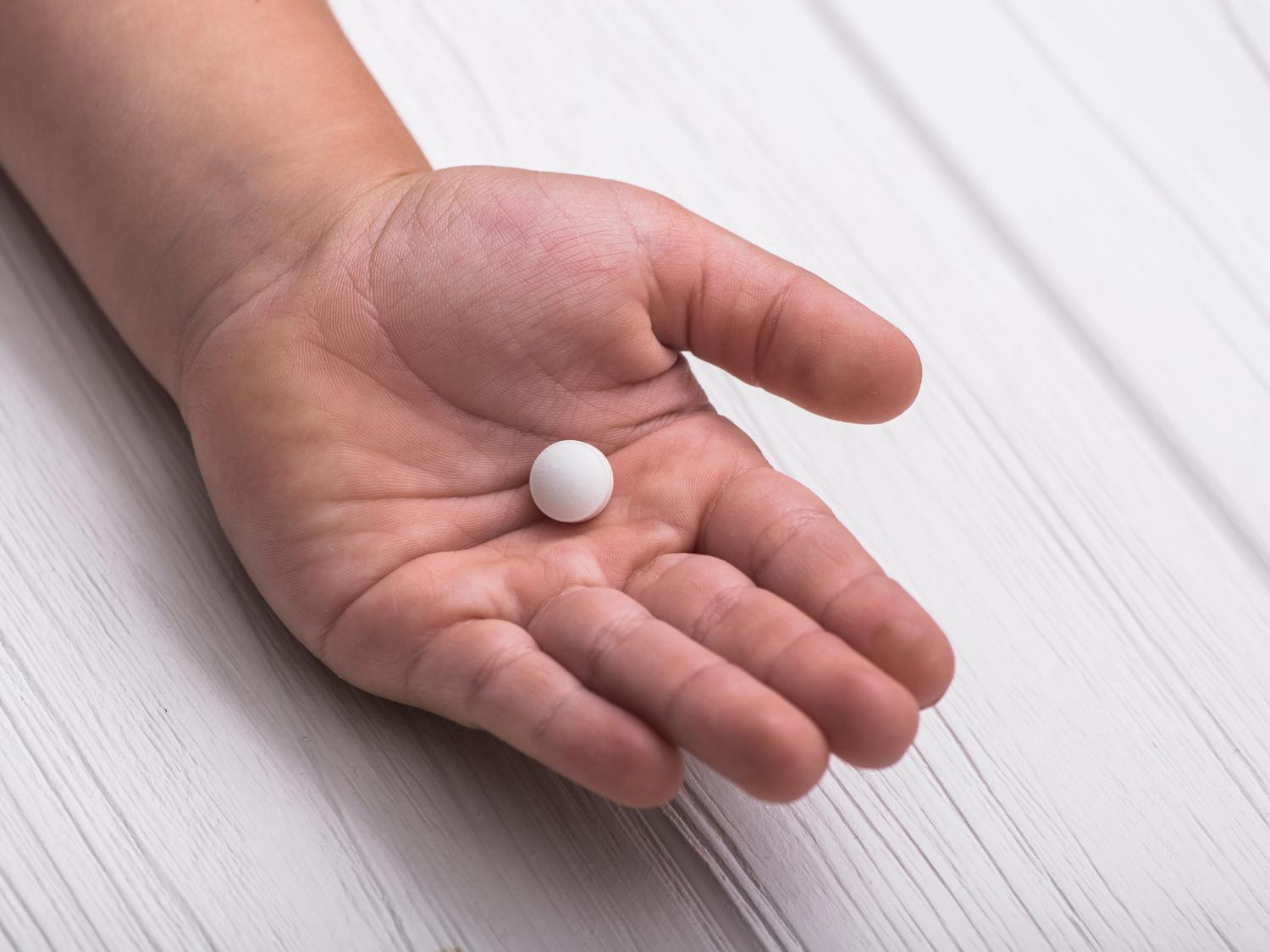 A child's hand holds a white pill