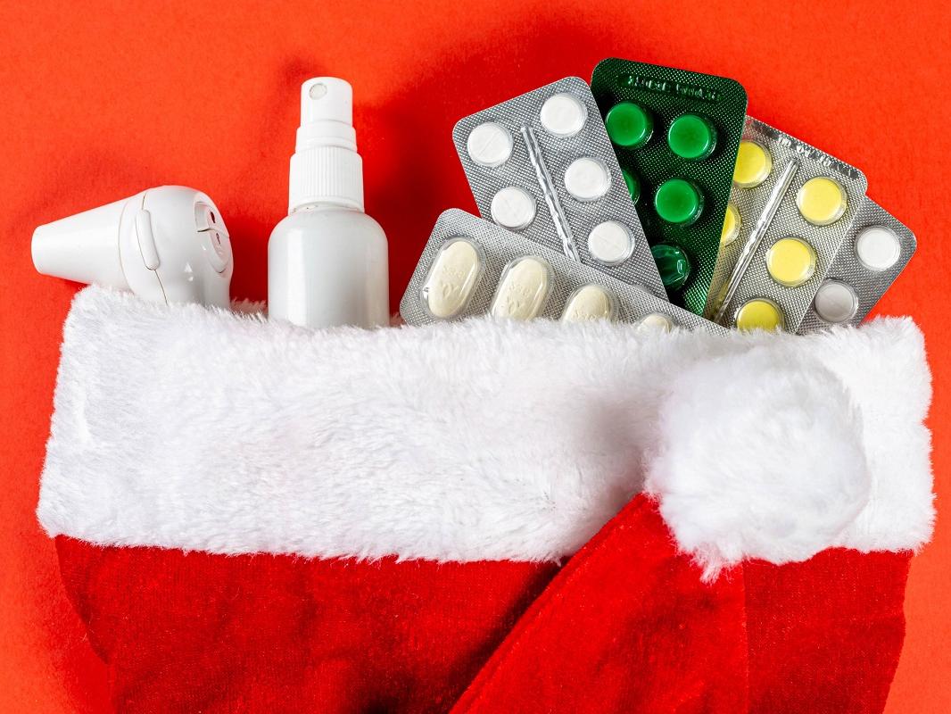Close-up of pills, thermometer and antiseptic in a Santa hat on red background.