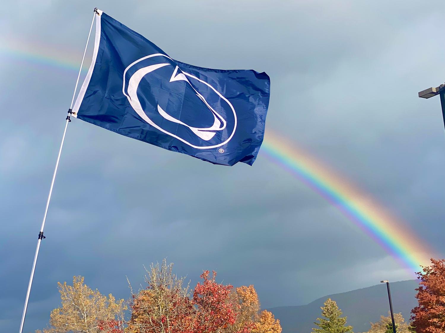 A Penn State flag with a rainbow in the background