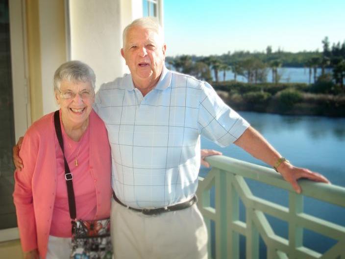 Man and woman standing on a sunny balcony overlooking a river.