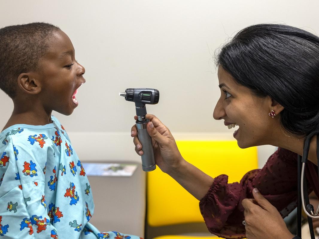 A physician uses a light to check the throat of a child.