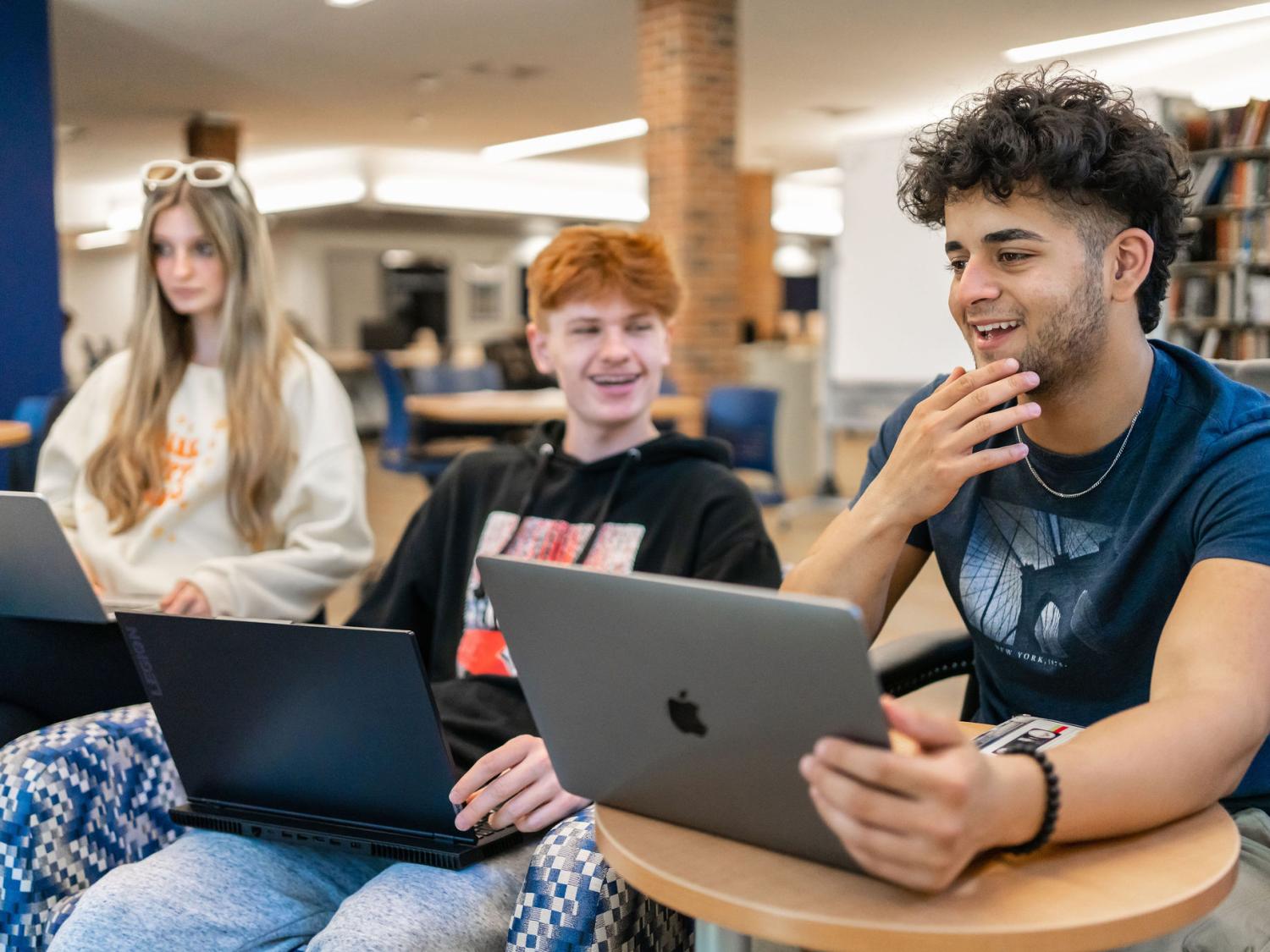 Three students seated and laughing in conversation with each other in a library.