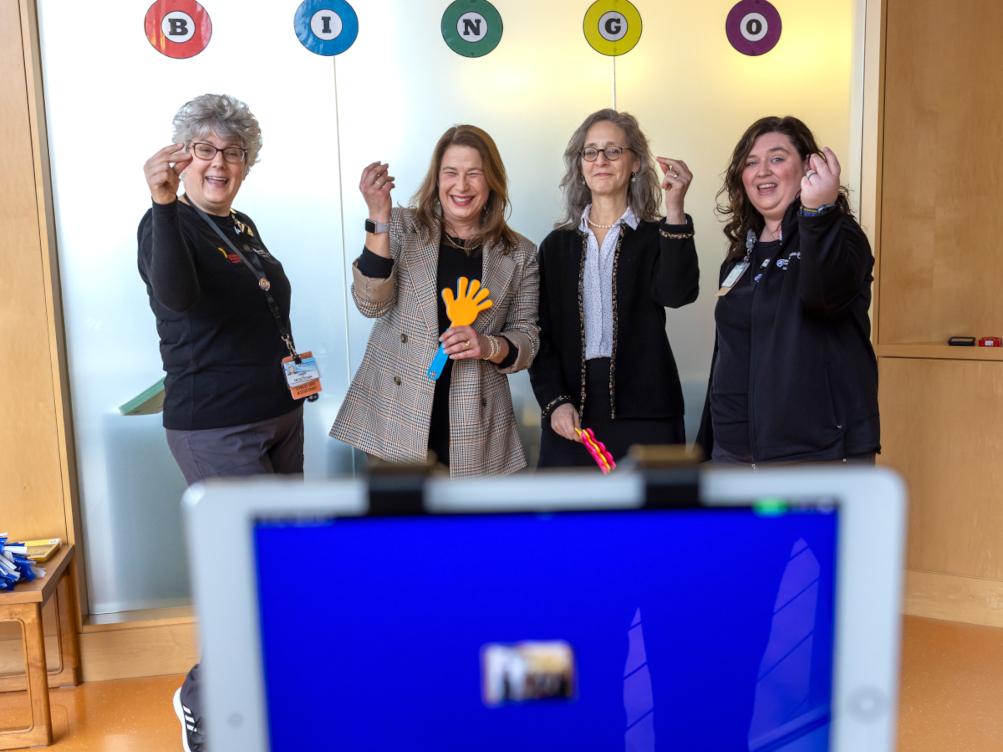 Four women stand in front of a screen, playing bingo