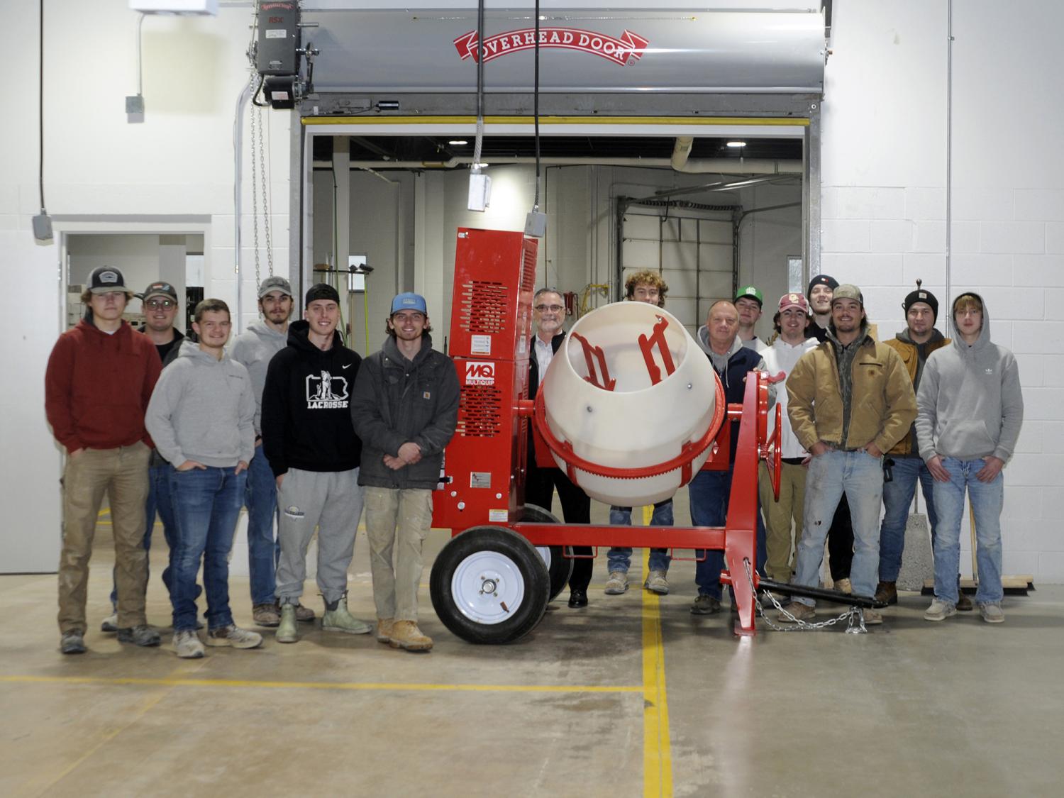 A group of people stand alongside a red and white concrete mixer.