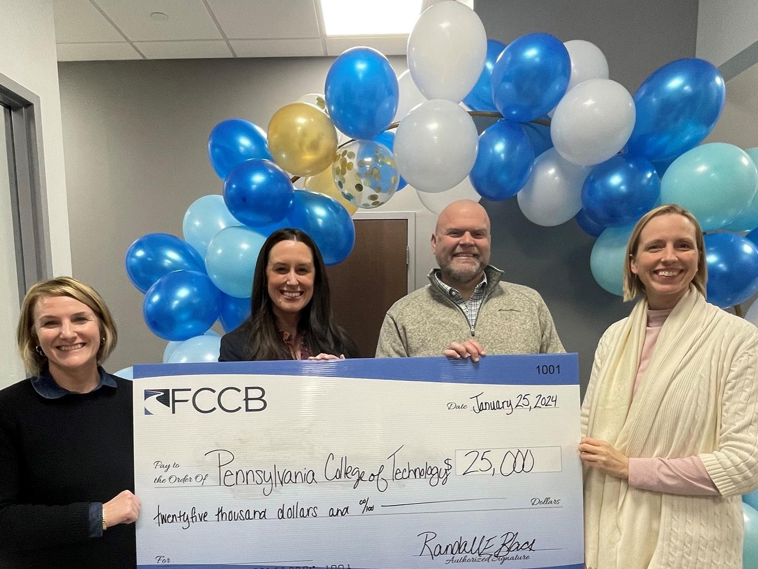 A group of people hold a large check with blue and white balloons in the background.