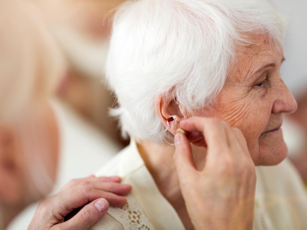 Female doctor applying hearing aid to senior woman's ear.