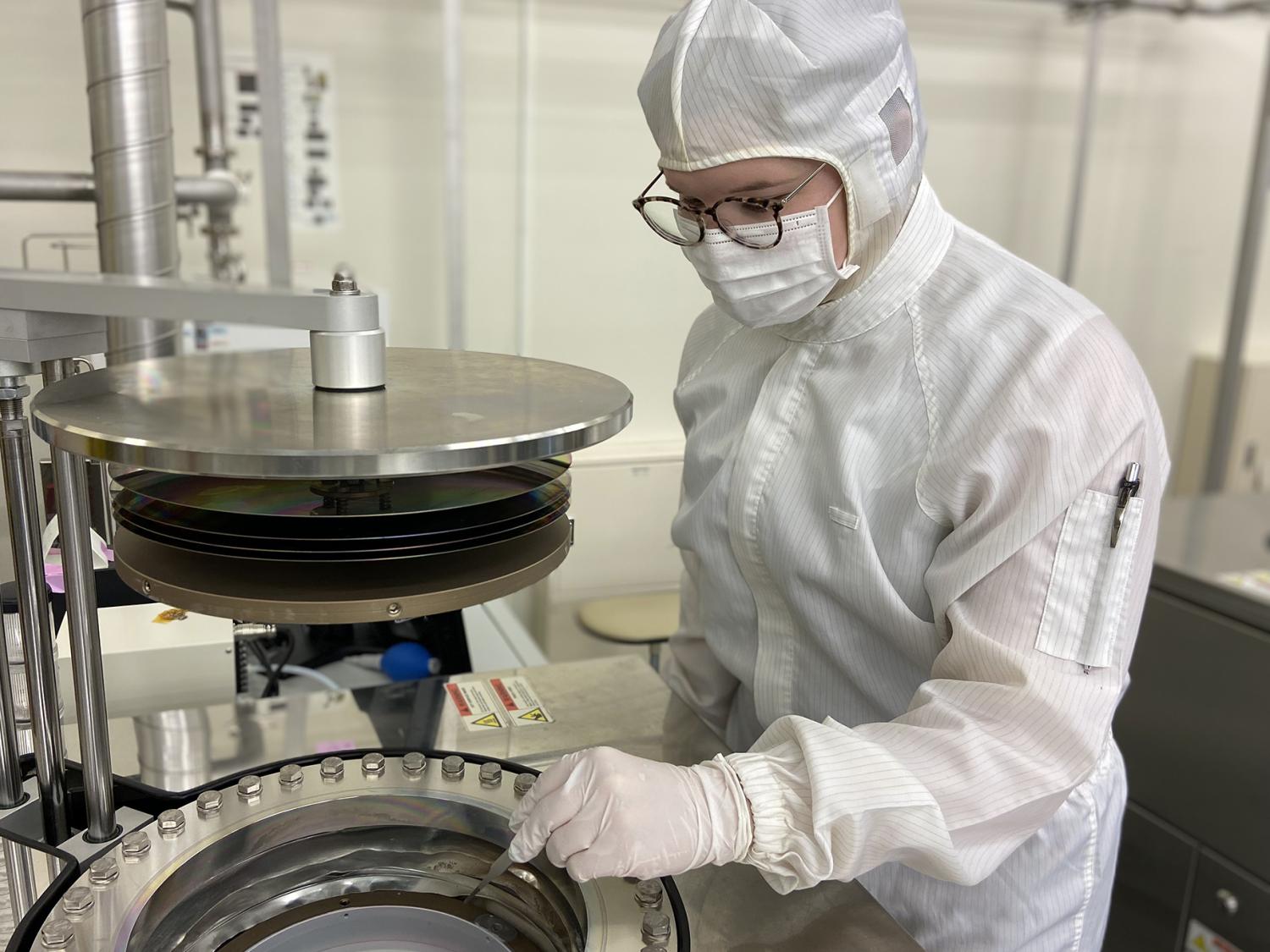 Person wearing white personal protective equipment works with laboratory equipment. 