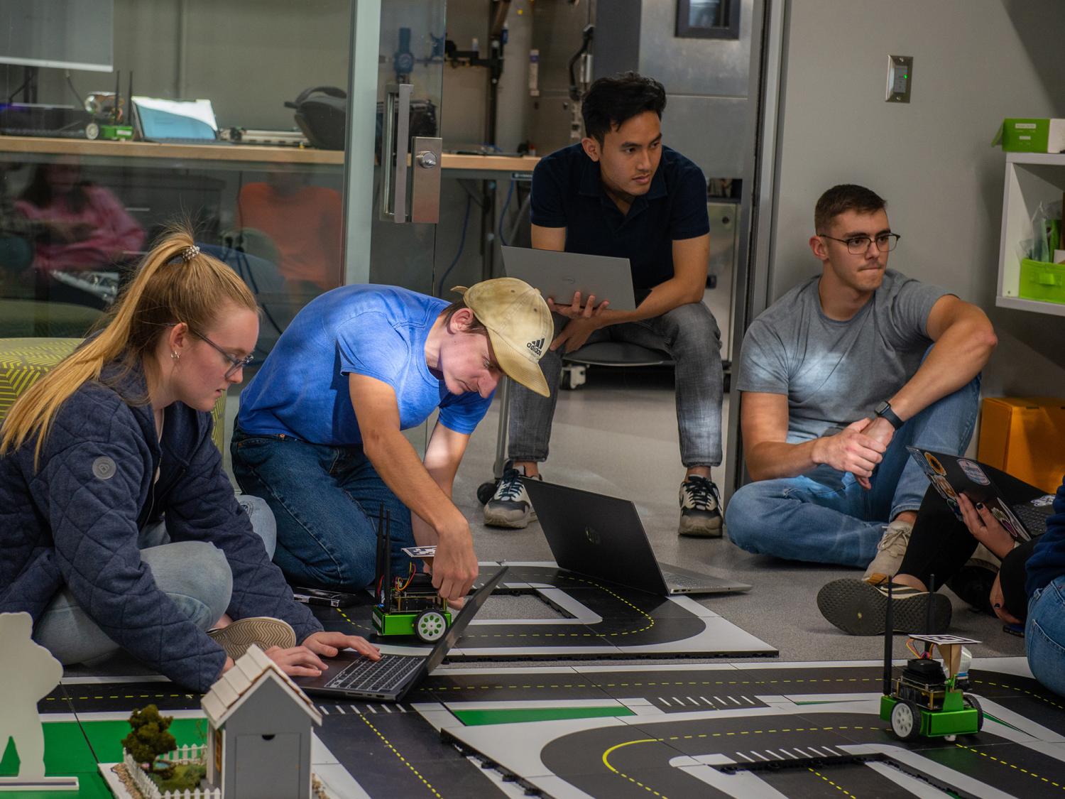 Four students collaborate on a remote vehicle running on a small track.