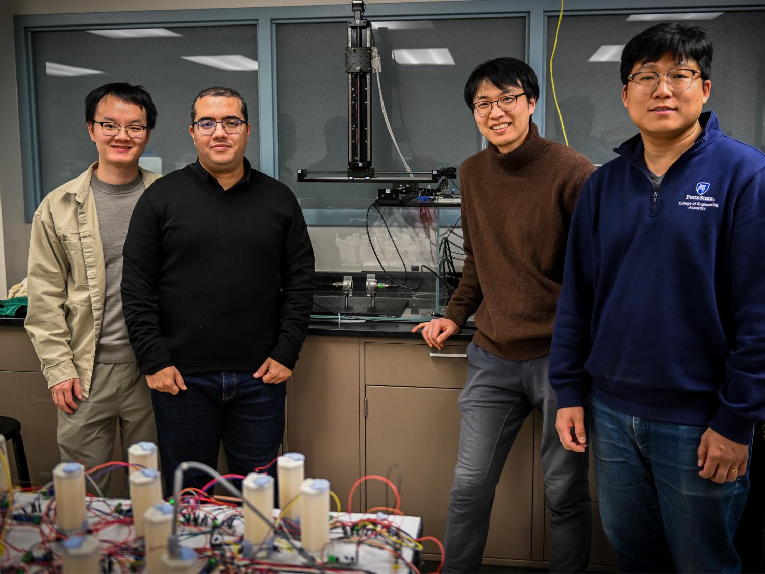 Four individuals pose near ultrasound lab equipment in a lab.