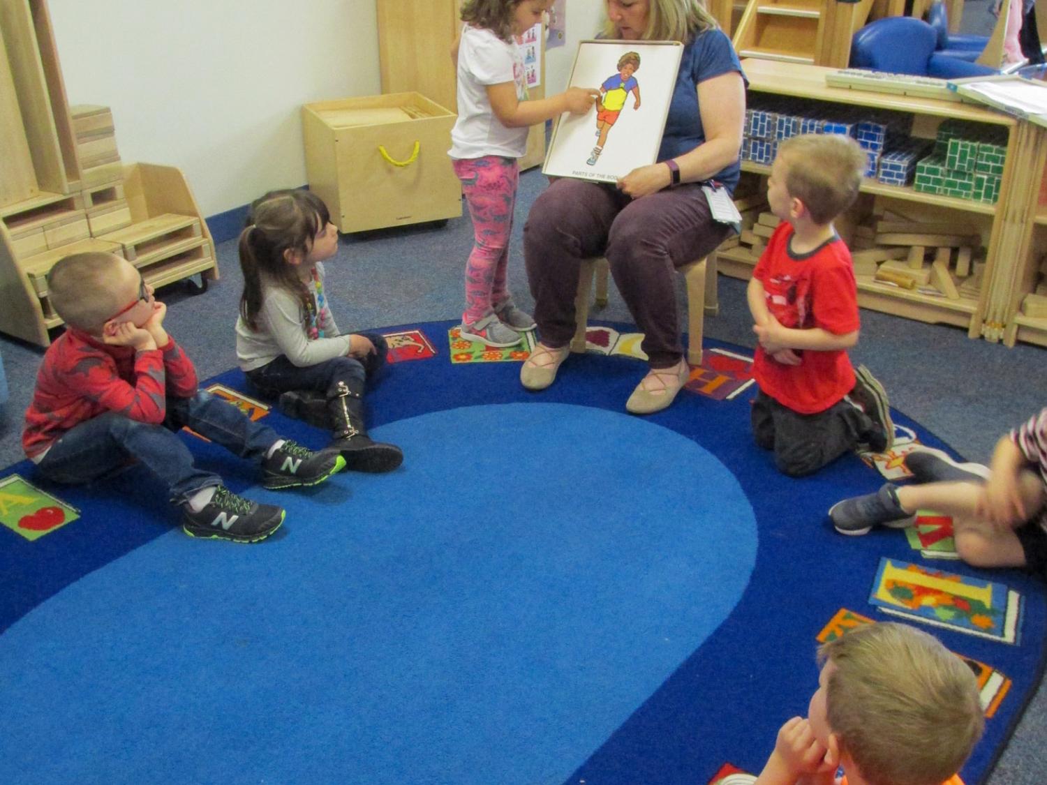 Children sit around a table in a learning center, listening to an adult talk to them