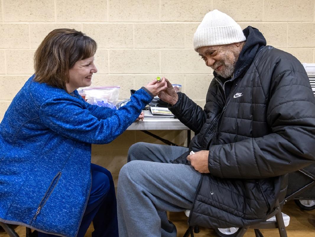 A man in a coat and winter cap reaches across a table and touches the hand of a woman in a coat. Both smile at one another.