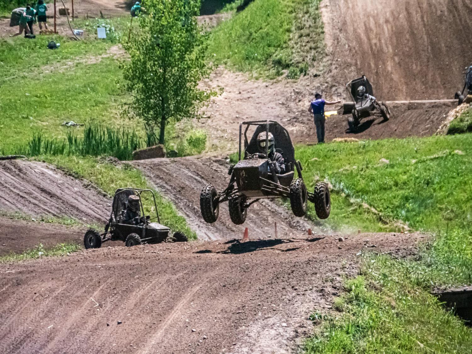 A baja vehicle elevates off the ground while racing on a dirt racecourse.