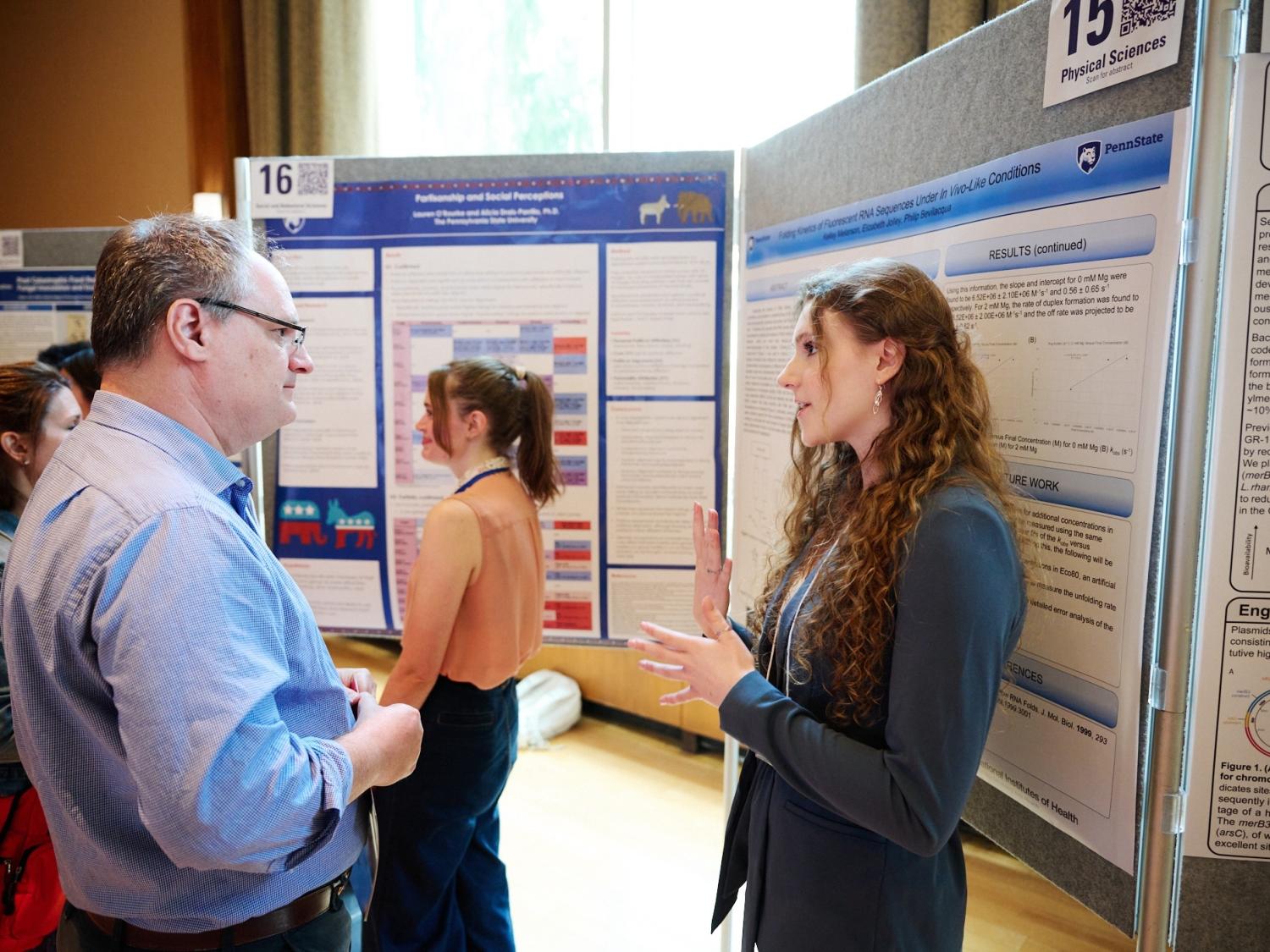 Faculty judge hearing explanation from student presenter in front of a research poster