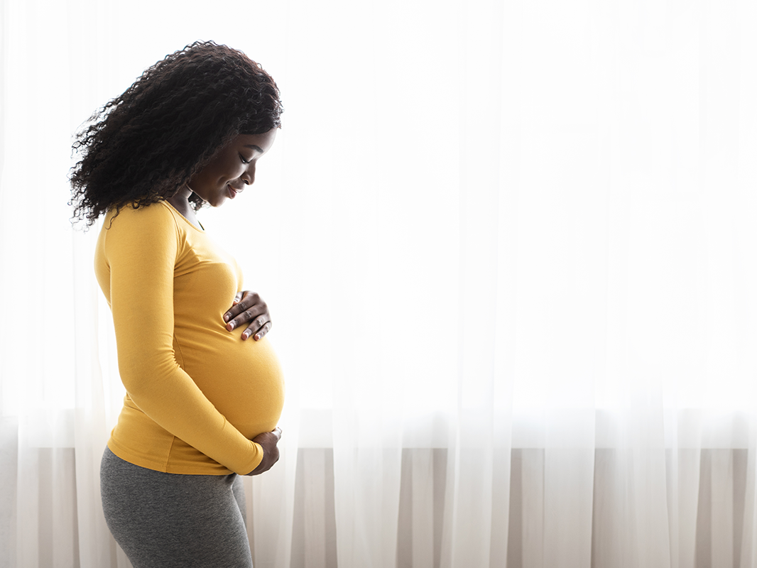 Black pregnant woman standing by window with hands on her belly