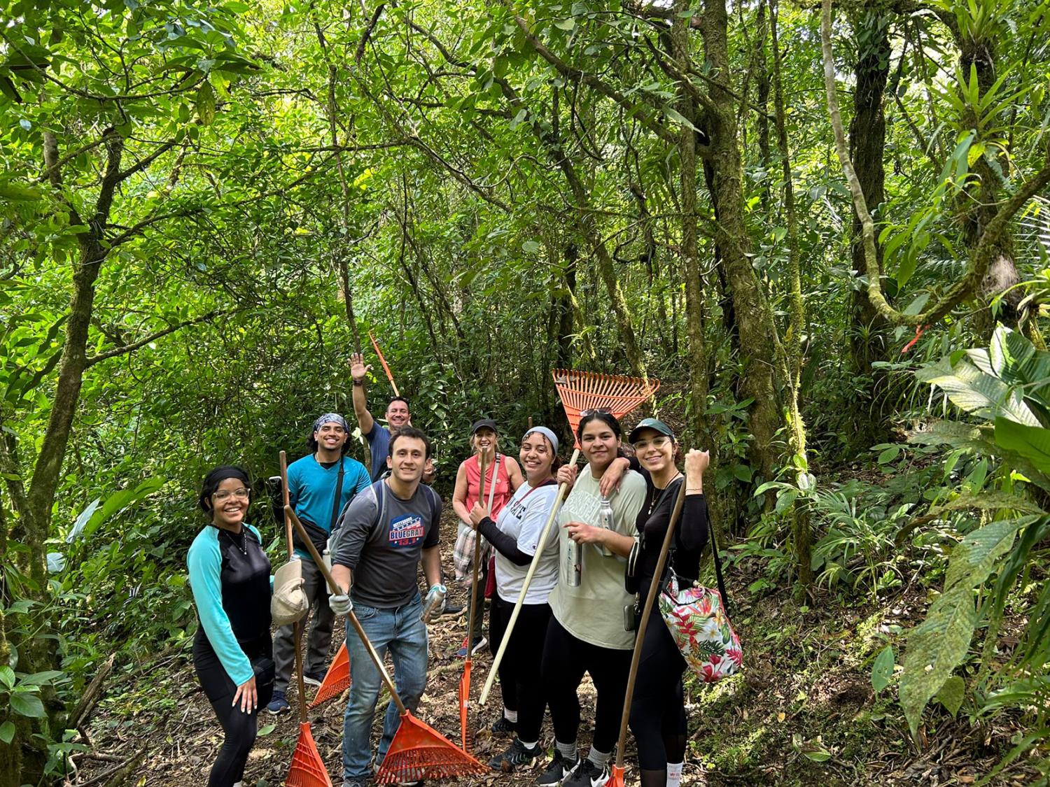 Group of students hold rakes while standing in the rainforest