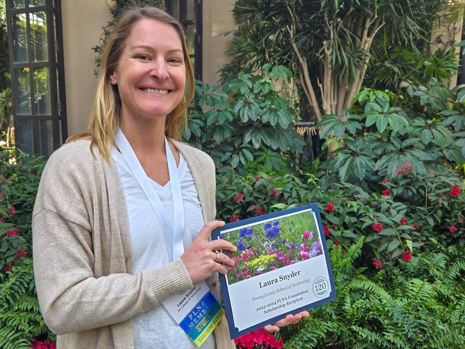 Laura Snyder holding her scholarship award with green landscaping in the background.