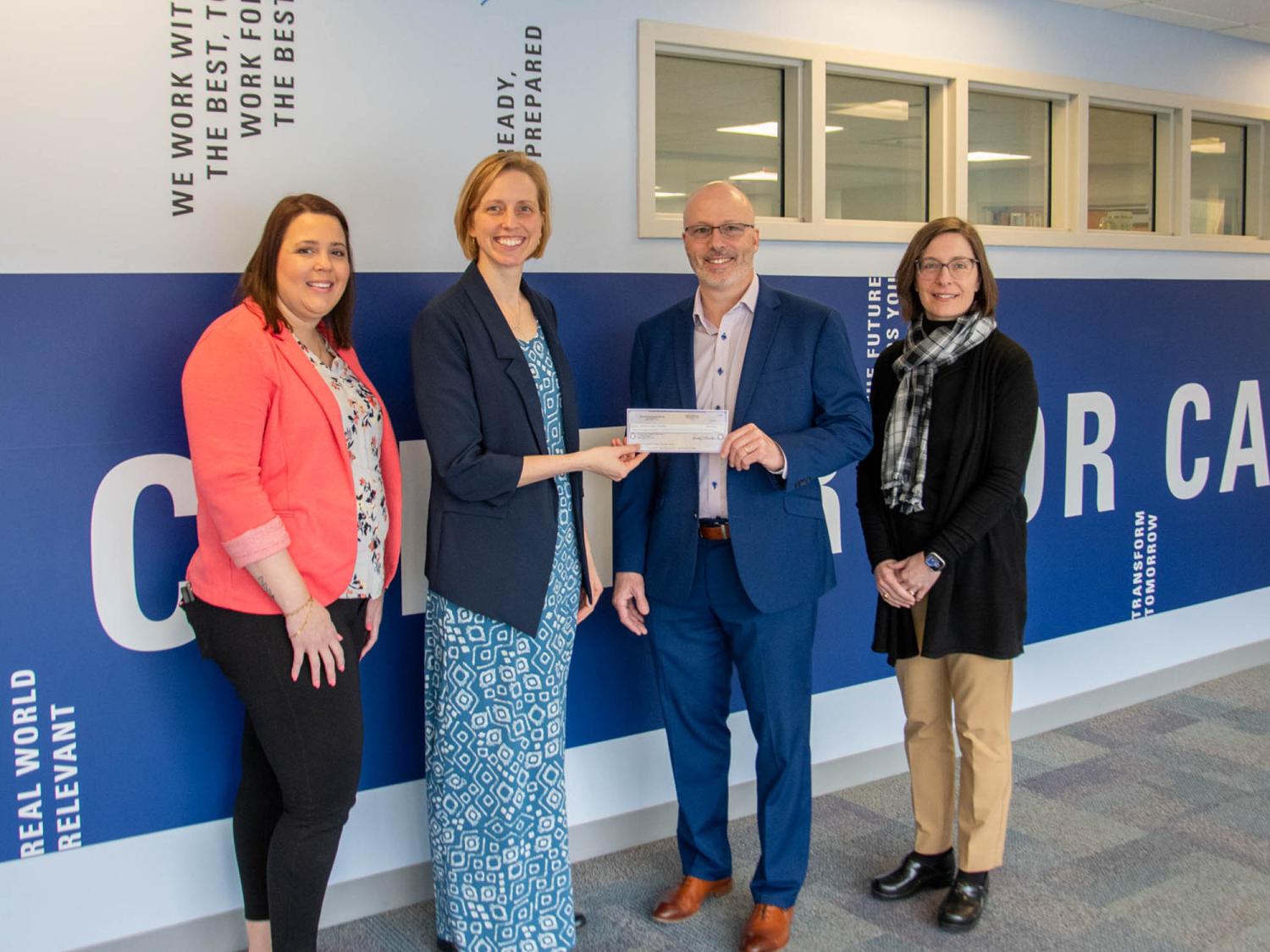 A group of people standing in a line agaist a blue and white wall. The two people in the middle are holding a check.