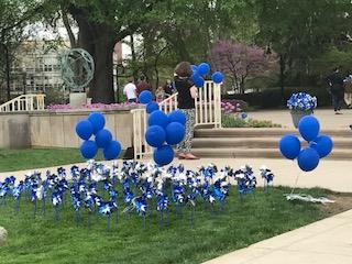 Blue and white pinwheels are stuck into a patch of lawn in front of blue balloons and a set of stone stairs.