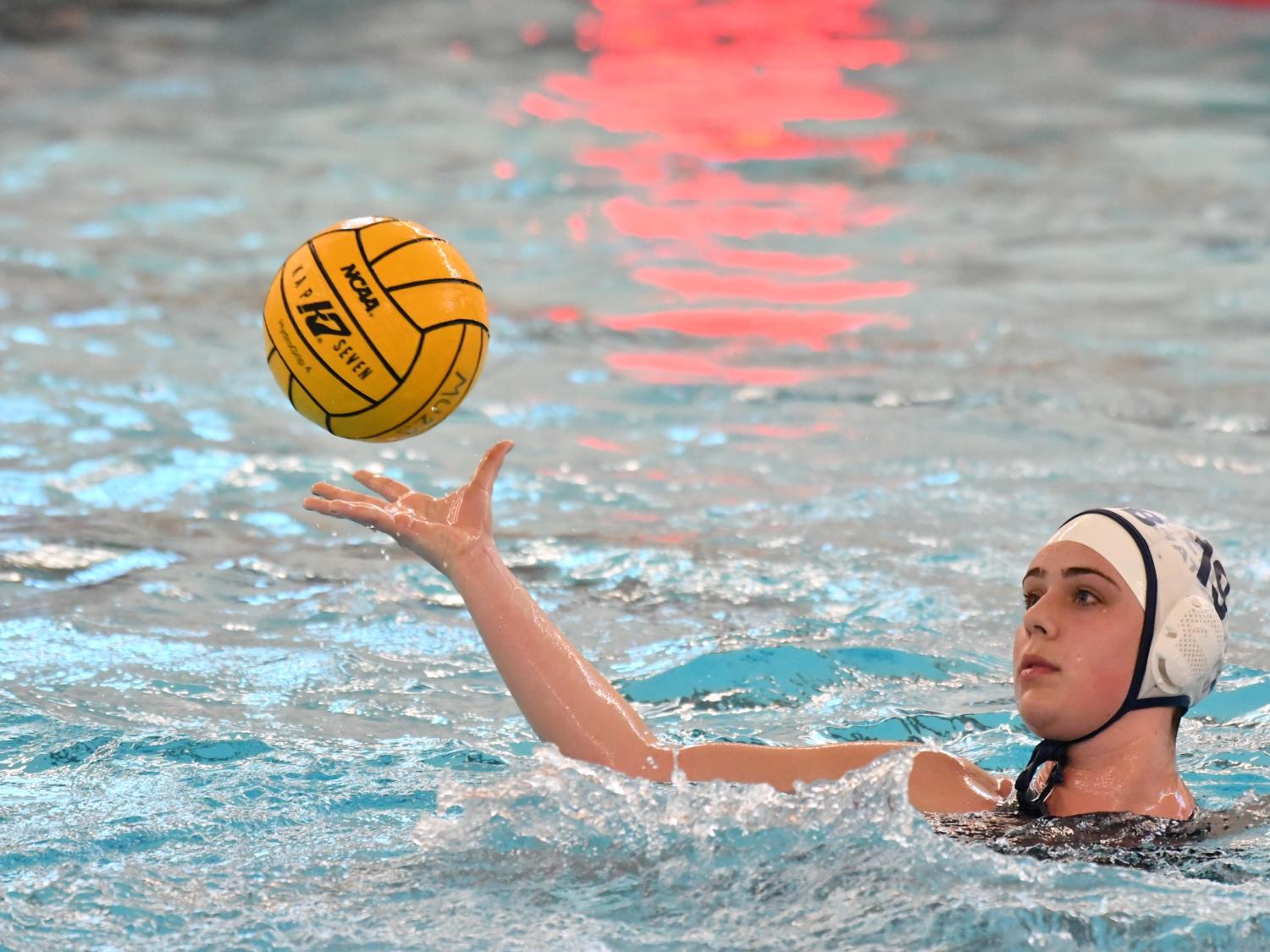 A female water polo player catches the ball while treading water.