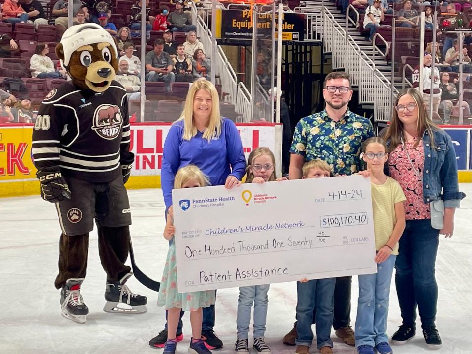 A check presentation happens on the ice at an ice hockey game. People are gathered around a big check smiling.