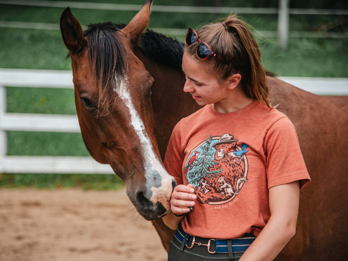 Gillian stands her a bay horse with its head over her shoulder