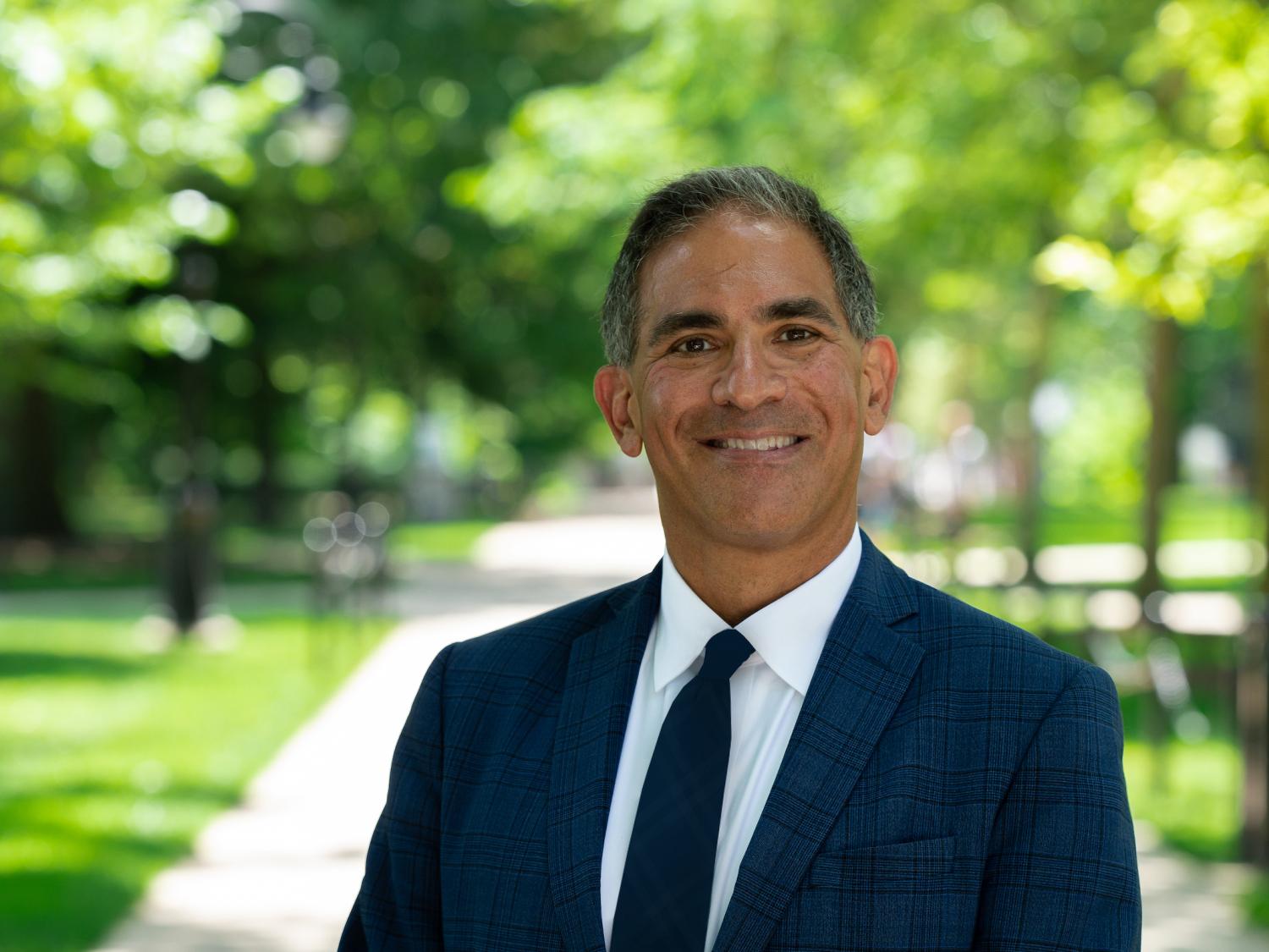 Justin Schwartz smiles and stands outside with green trees in the background.