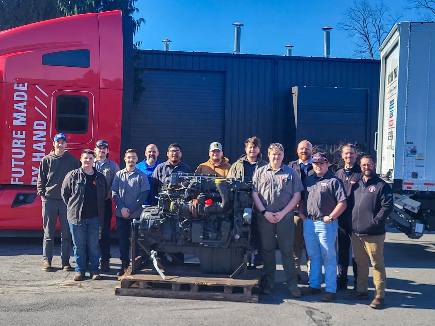 A group of students and faculty pose for a photo in front of an engine