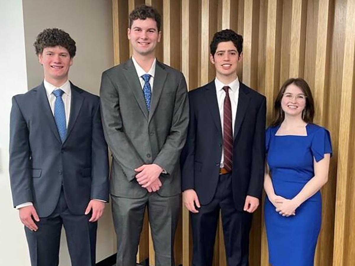 Three male students and a female student stand posing for a picture