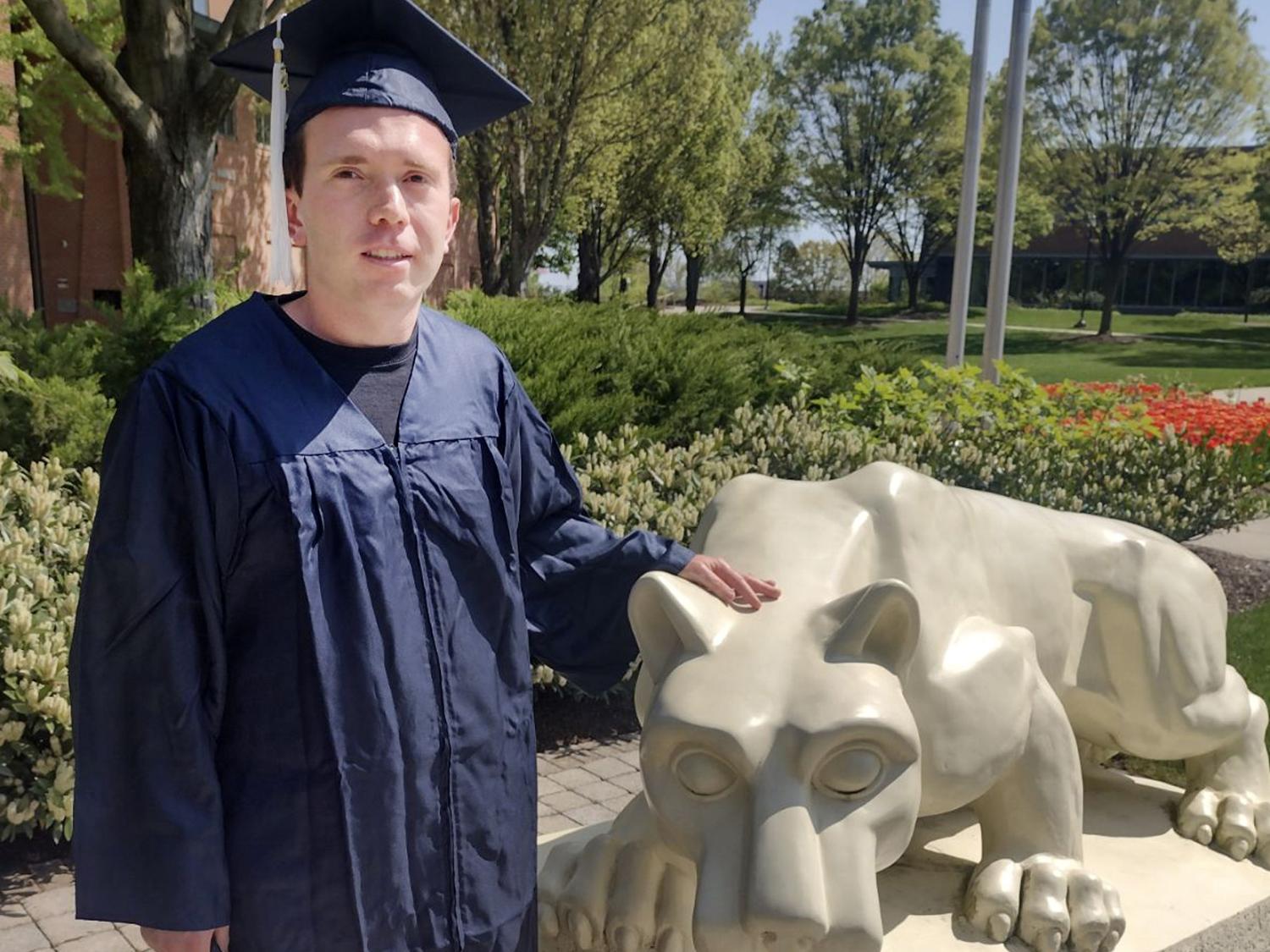 Nick Spohn in commencement regalia with Lion Shrine at Penn State Harrisburg