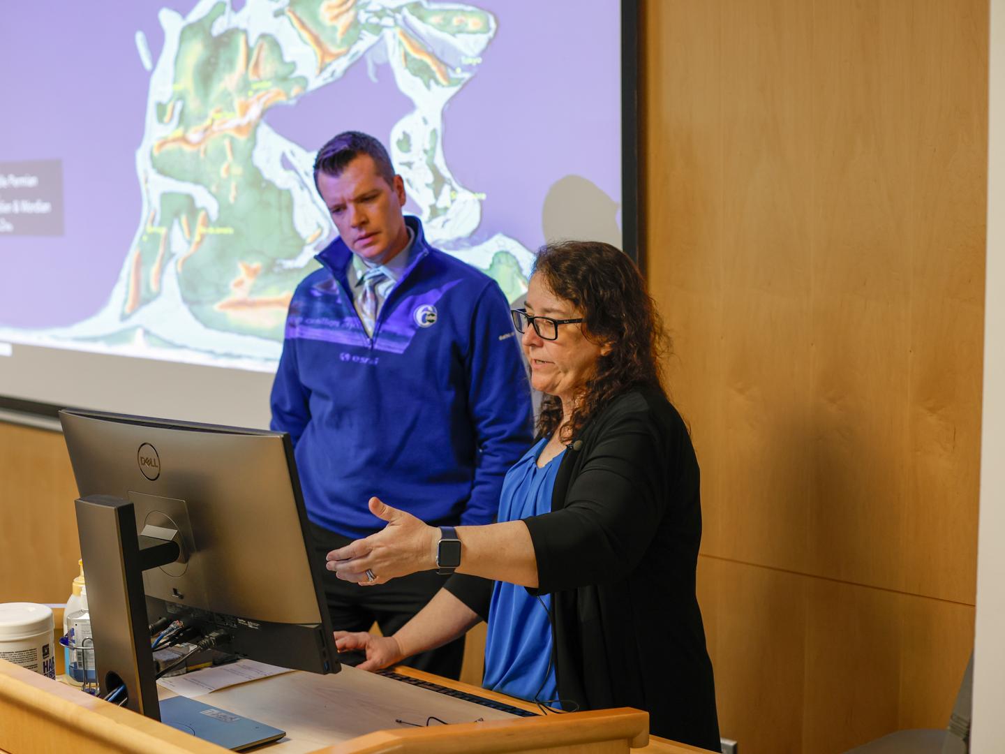 A professor points to a computer to explain an earthquake to a television news reporter.