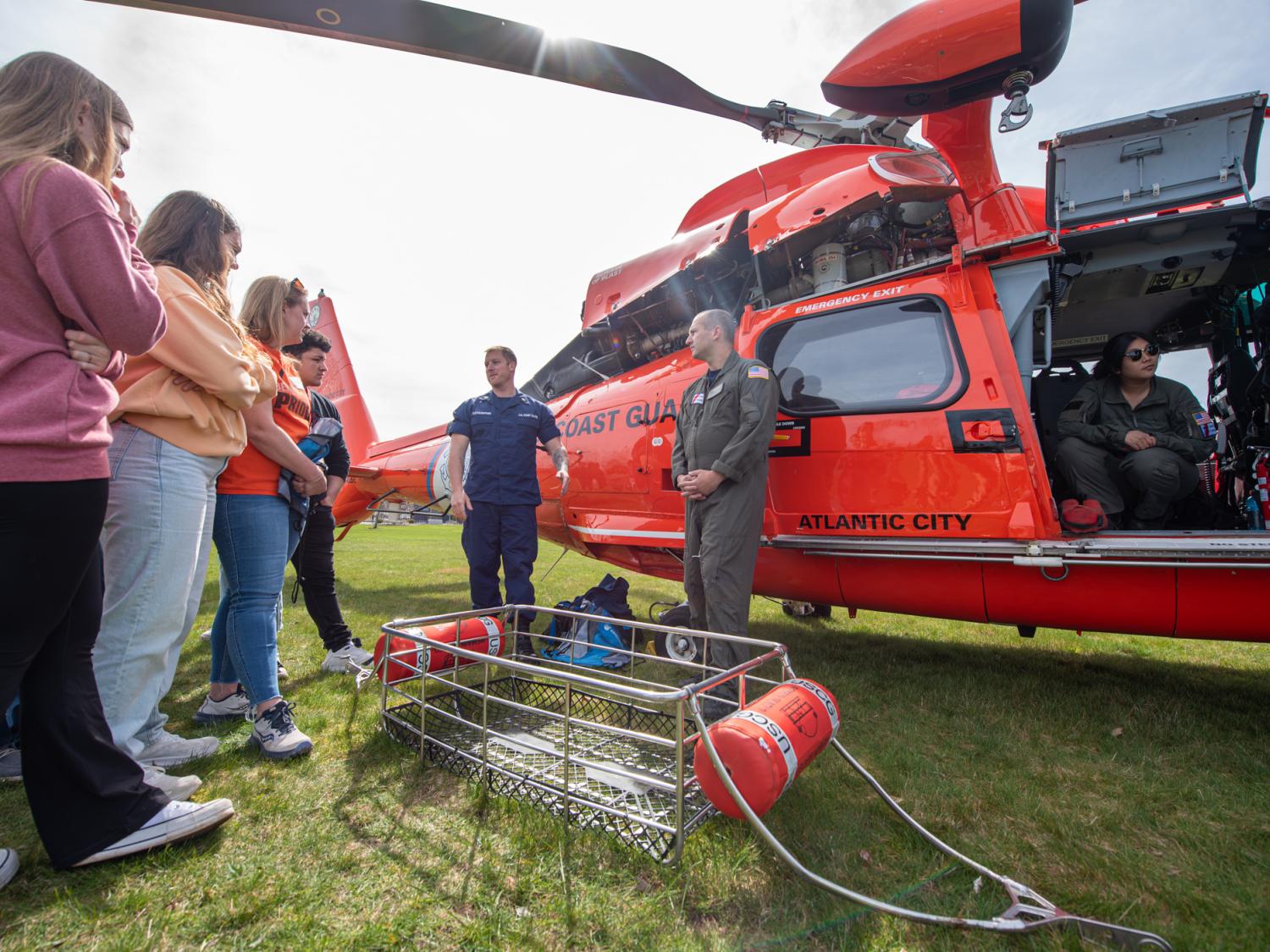 A group of people stand talking by a helicopter