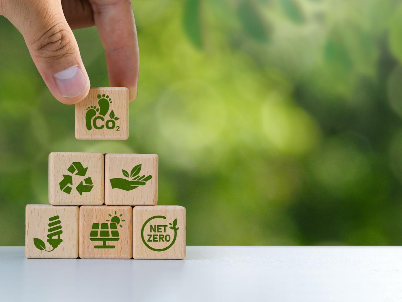 Stock image of person stacking wooden blocks decorated with green-energy icons.