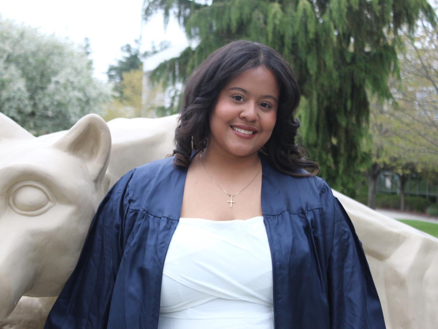 Aidee Santos Acosta poses in front of Nittany Lion Statue in grad gown