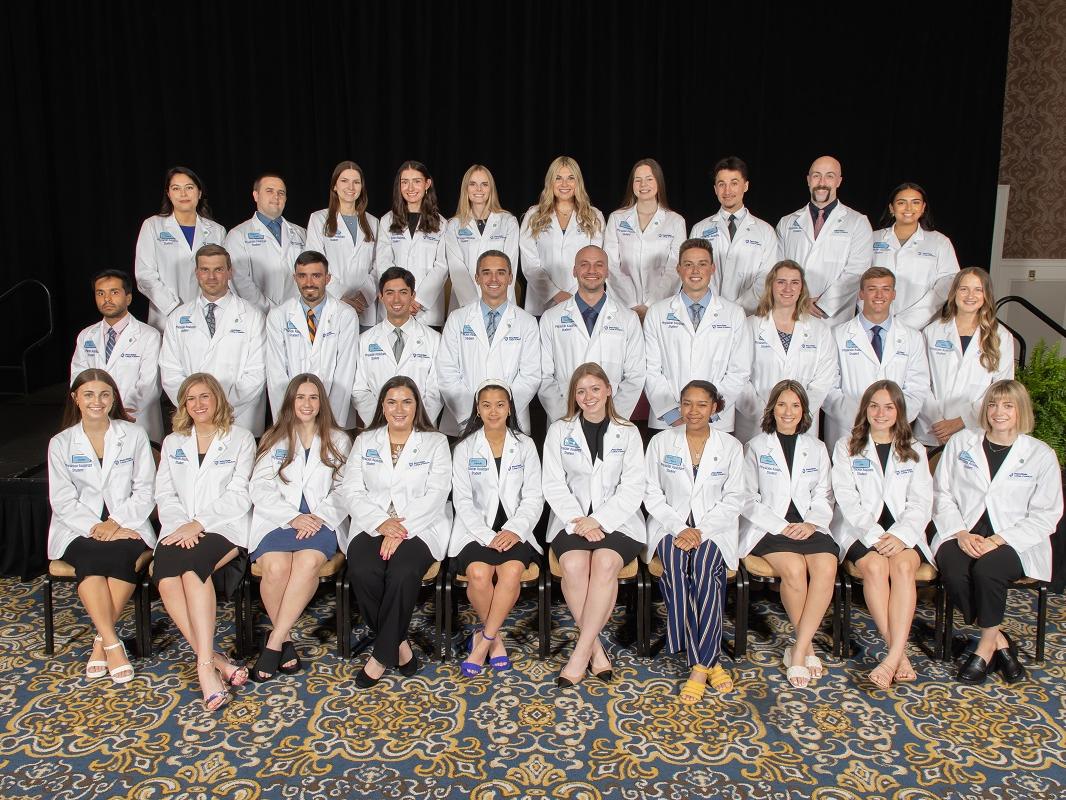 A group of students wearing short white coats, signifying their entry into the medical profession, pose for a photo