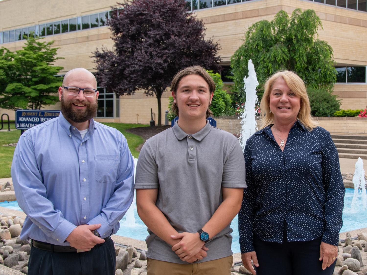 Three smiling people pose for a photo in front of a fountain