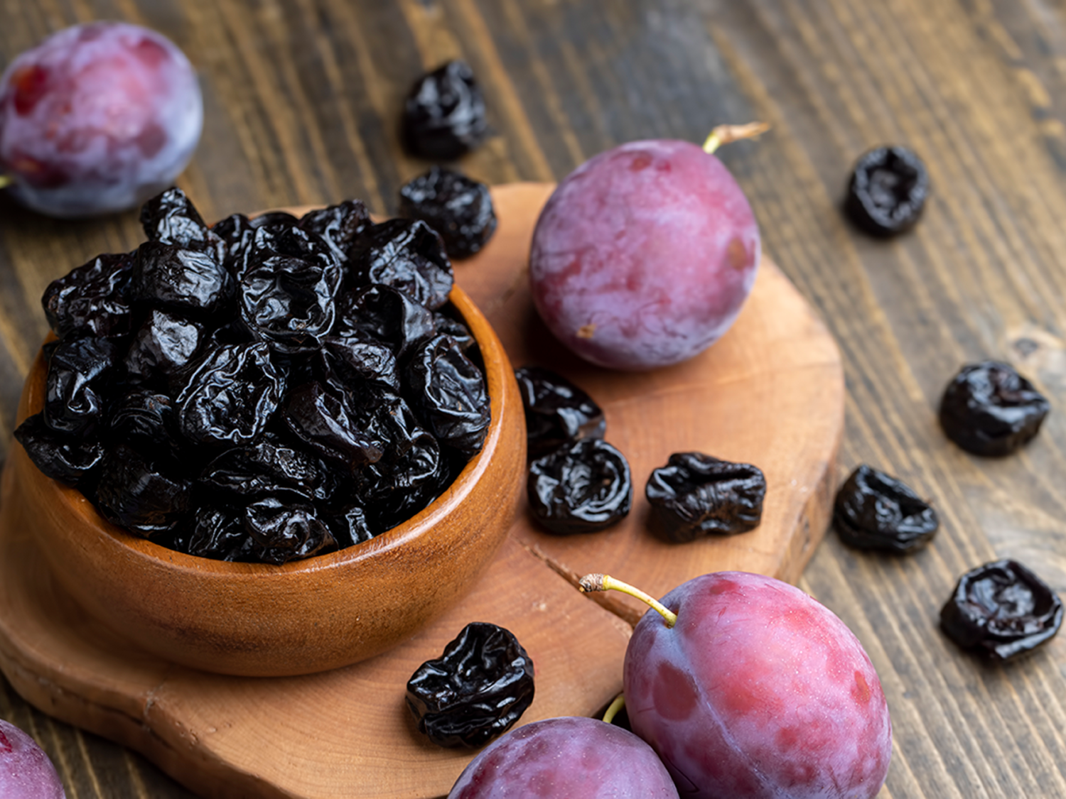 a pile of dried prunes and fresh plums on a wooden table
