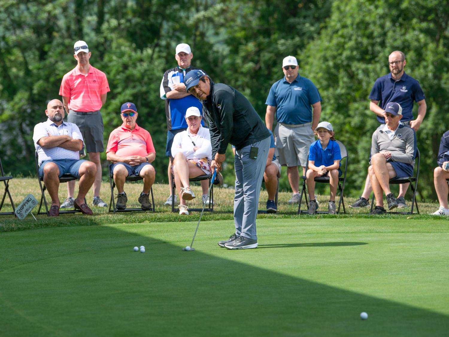 A man demostrates putting form on a golf course for spectators