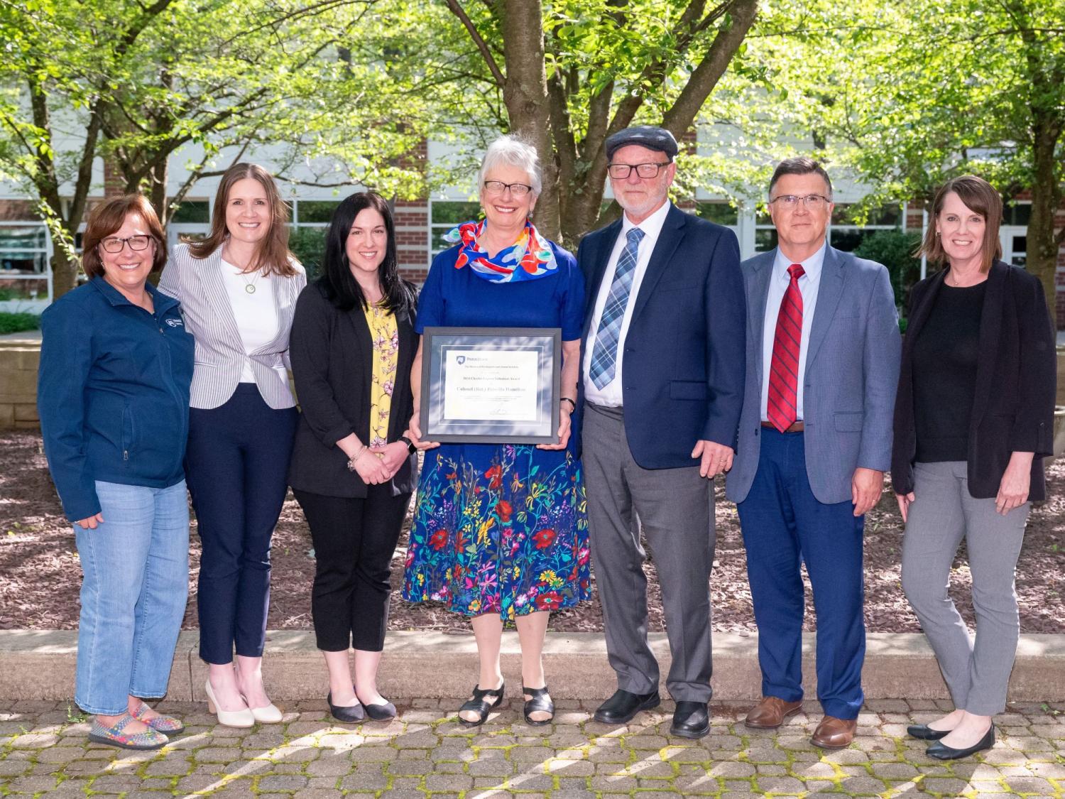 Seven people pose with framed certificate