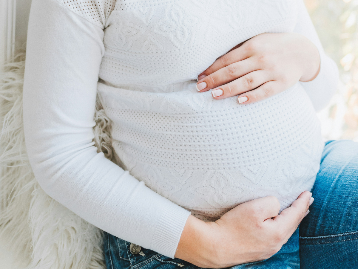 A pregnant woman in a white sweater rubbing her stomach
