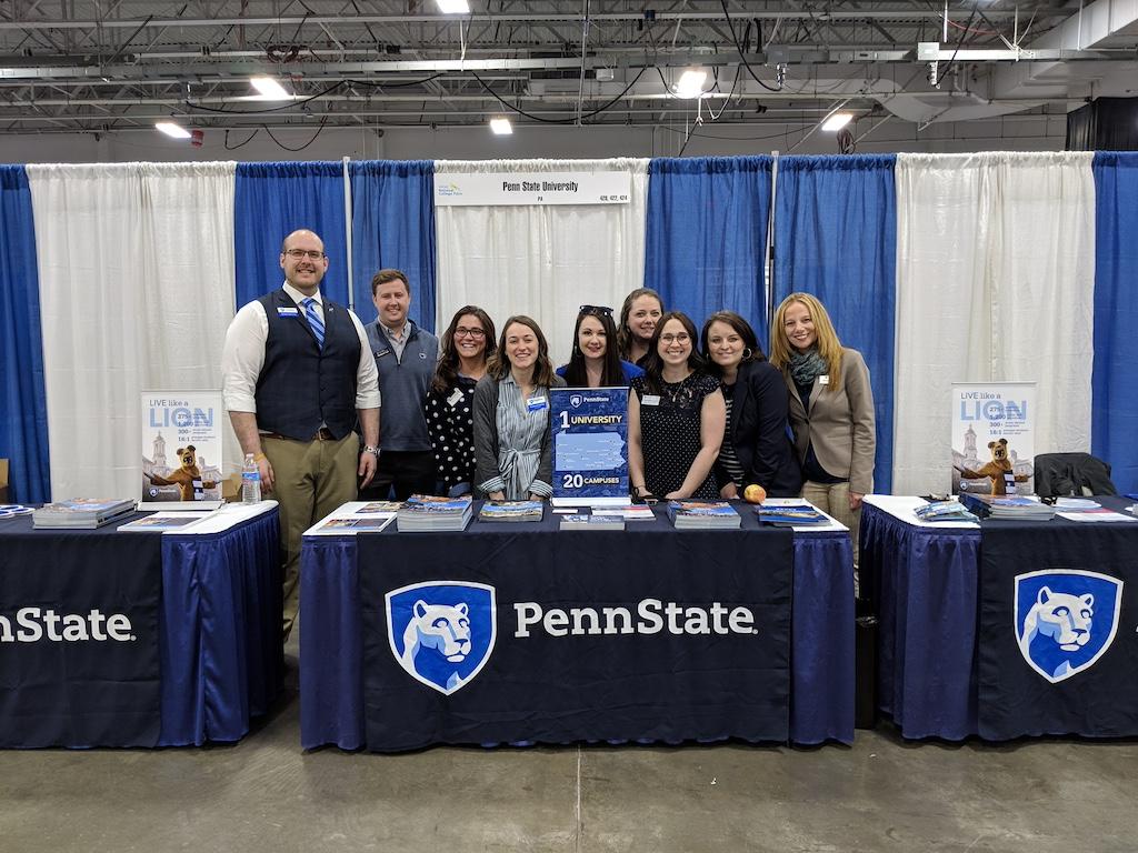 A group of people stand behind a table that reads "Penn State"