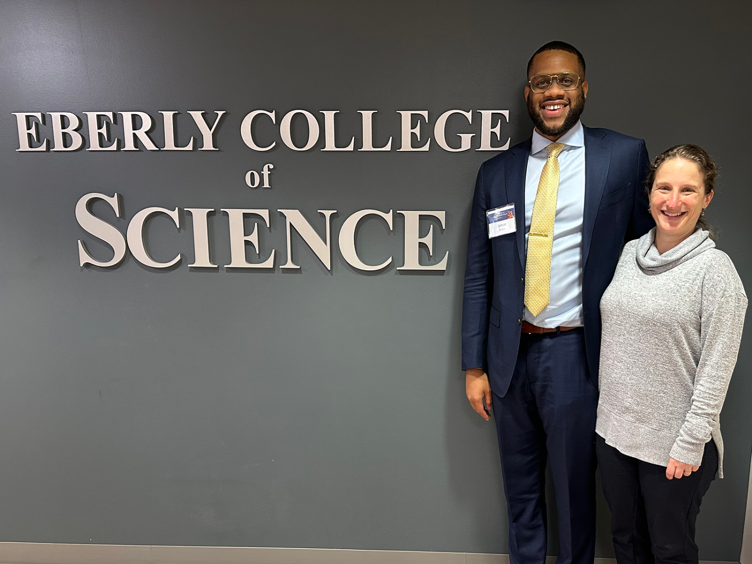 Two people stand to the right of a sign reading "Eberly College of Science"