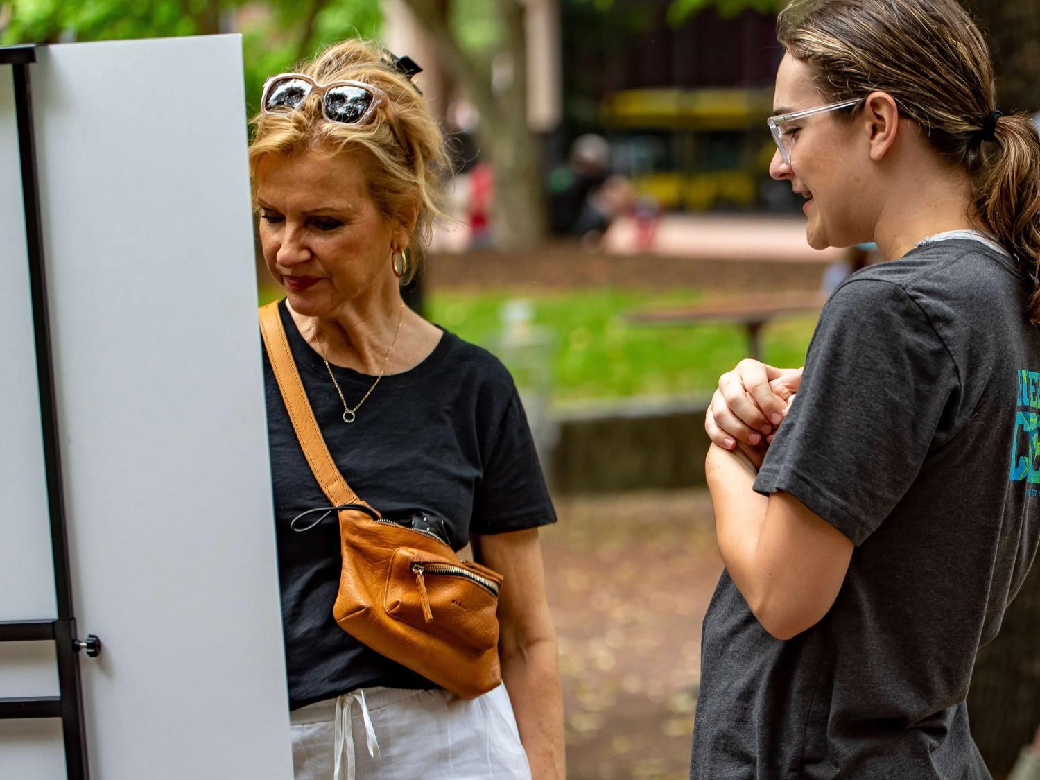 Two people looking at art propped up on an easel in a park.