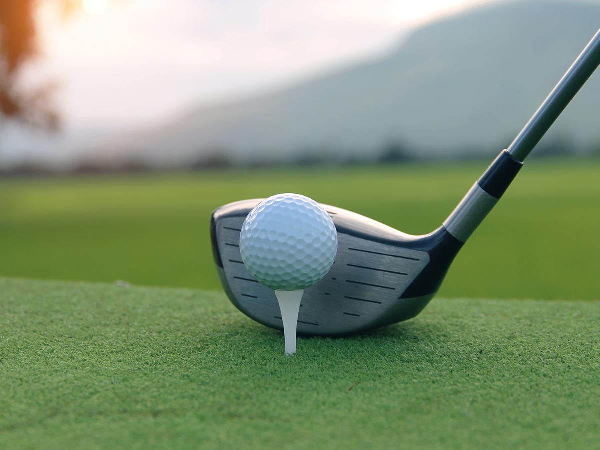 A golf ball on a tee with a golf club ready to hit it