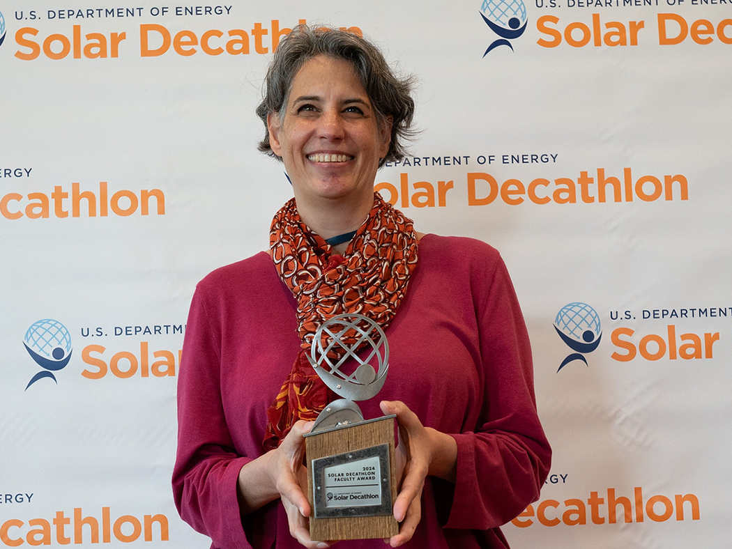 Lisa Iulo holding a trophy in front of a U.S. Department of Energy Solar Decathlon backdrop. 