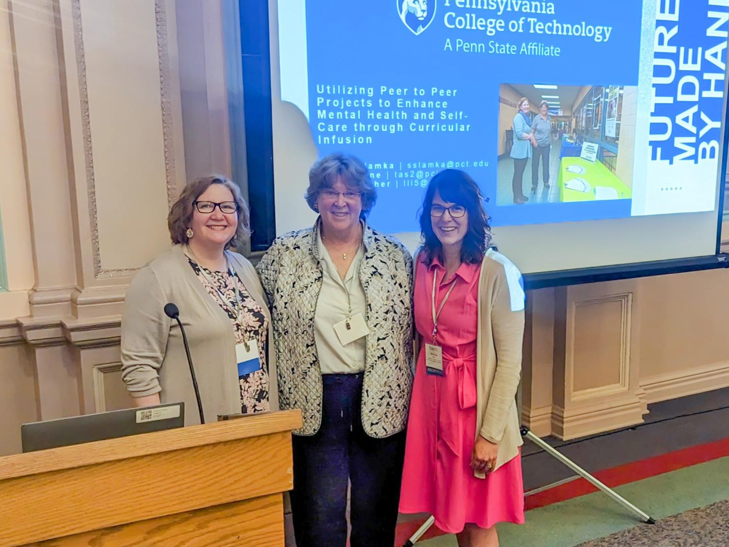 A trio of people pose for a photo in a conference center meeting room
